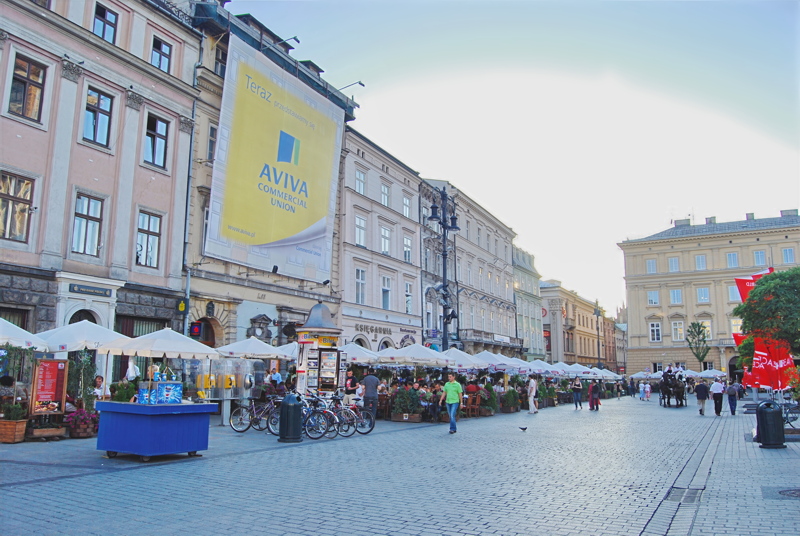 16 - The vibrant Plac Mariacki and adjacent historic streetscape in the Old Town of Kraków, Poland, featuring cobblestone paving, outdoor café seating, and traditional architecture